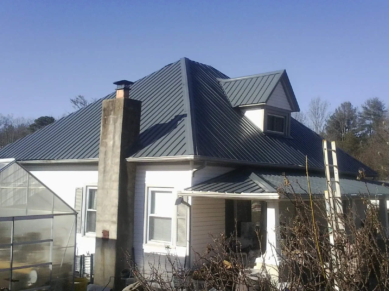Dark blue standing seam metal roof on a white farmhouse with dormer — Slate & Tile Roof Repair by Roofing Brothers in Garner