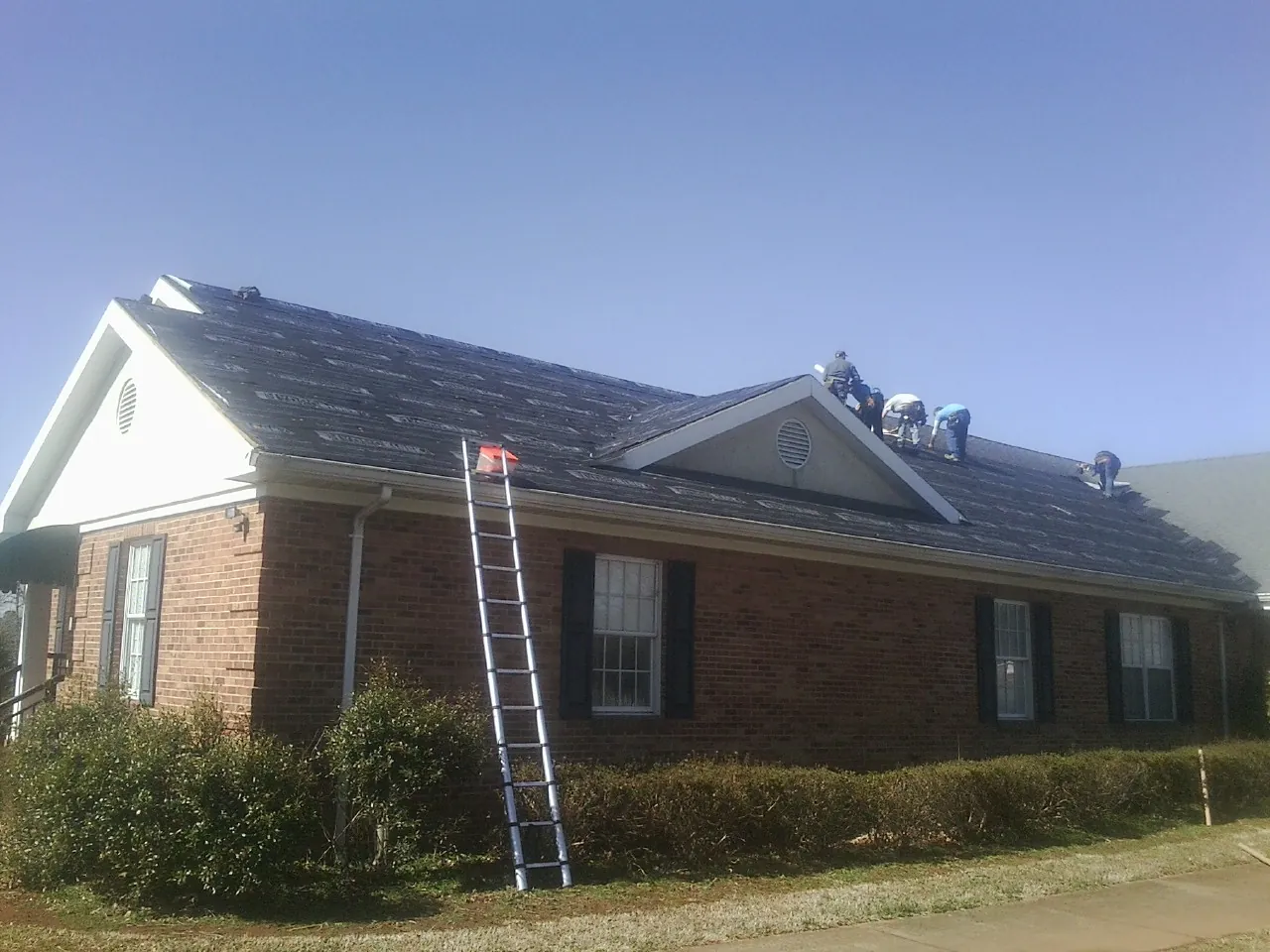 Crew tearing shingles off a brick ranch roof with a ladder set — Emergency Roof Repair work by our crew in Garner