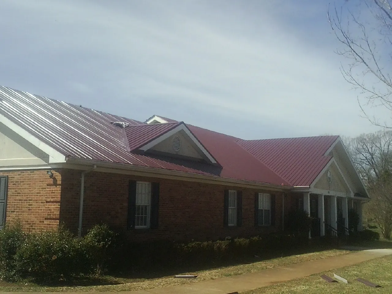 Red metal roof with gabled entries on a long brick building, from a Hail Damage Roof Repair job in Garner