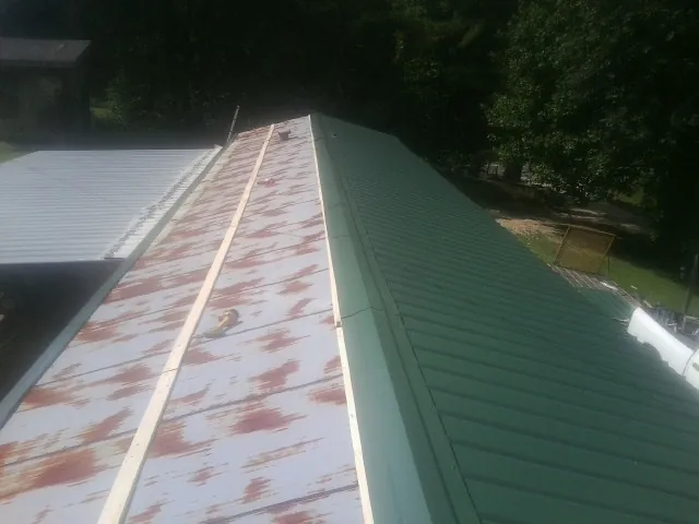 Old rusted panels beside newly installed green metal roofing — Wind Damage Roof Repair by Roofing Brothers in Garner