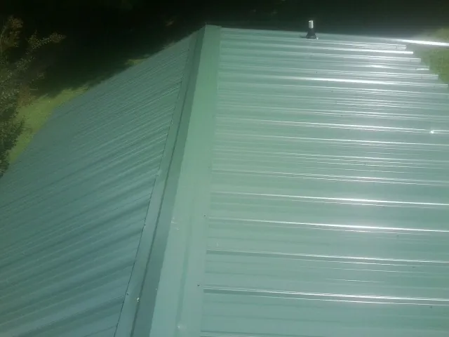 New green metal panels meeting at the ridge of a roof — Flat Roof Repair work by our crew in Garner