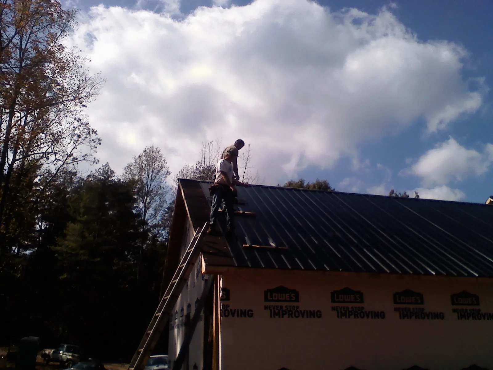 Roofer fastening dark metal panels high against a cloudy sky, from a Roof Inspection job in Garner