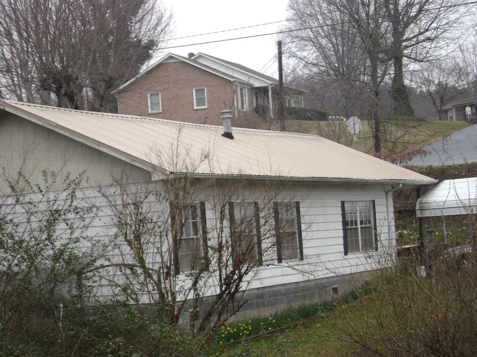 Tan metal roof on a white sided house set into a hillside — Commercial Roofing by Roofing Brothers in Garner
